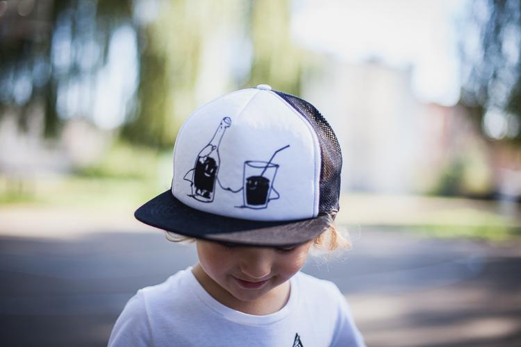chłopiec w białej czapce z daszkiem czarnym printem stoi na boisku do street ball