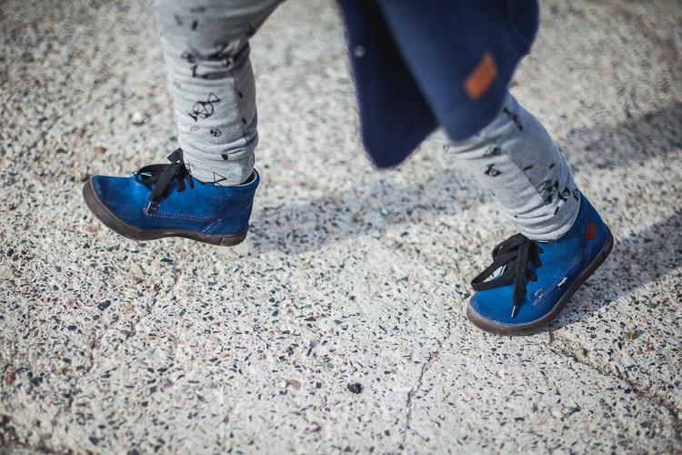 chłopiec w niebieskich zamszowych butach i szarych legginsach biegnie po betonowej płycie