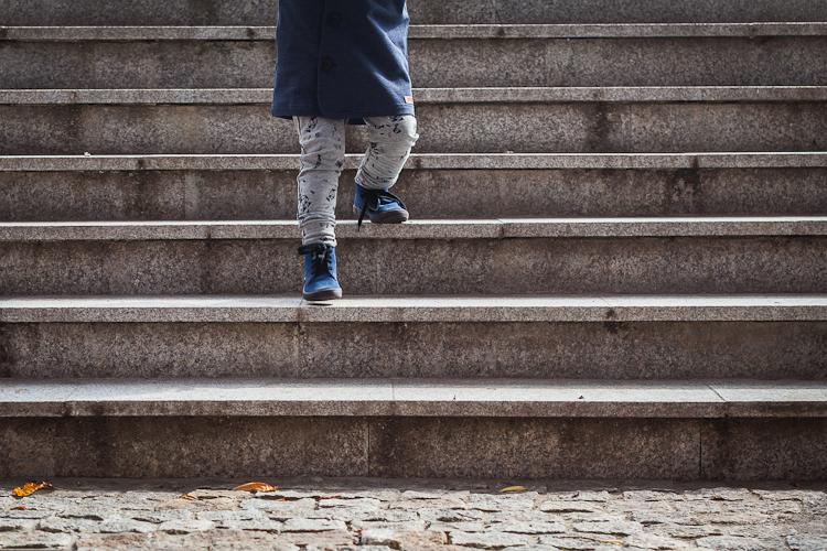 chłopiec w zamszowych bucikach i szarych legginsach kukukid schodzi po kamiennych schodach