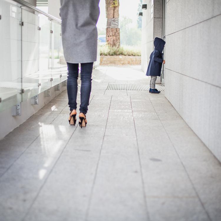chłopiec w płaszczu z kapturem spaceruje z mamą ubraną w szary płaszcz oversize i czarne rurki po chodniku nowego osiedla Garnizon