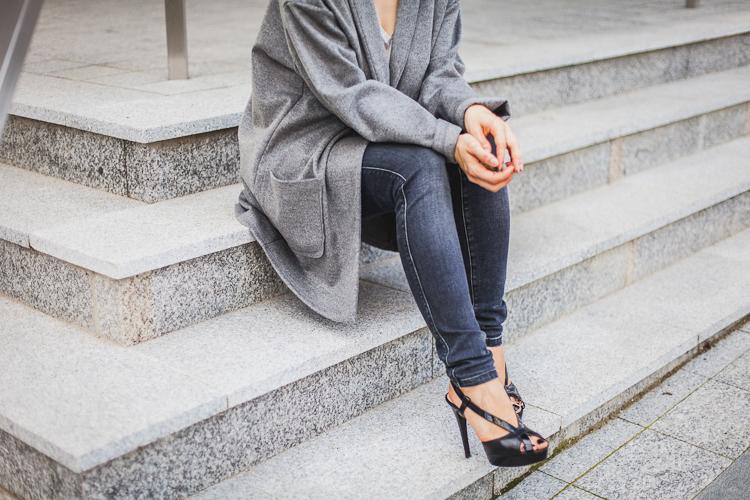 dziewczyna w szarym płaszczyku z wełny siedzi na kammiennych schodach I girl in grey coat and black jeans