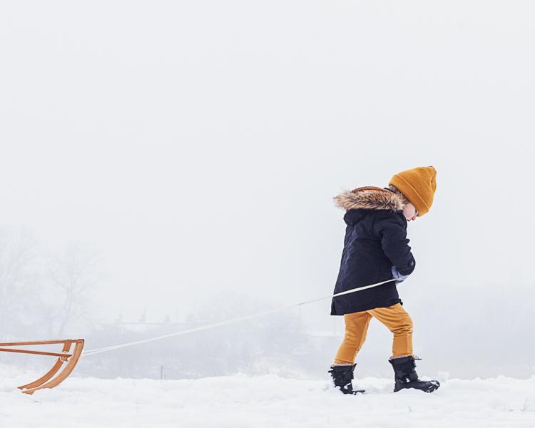 mały chłopiec spaceruje po śniegu ciągnąc za sobą sanki